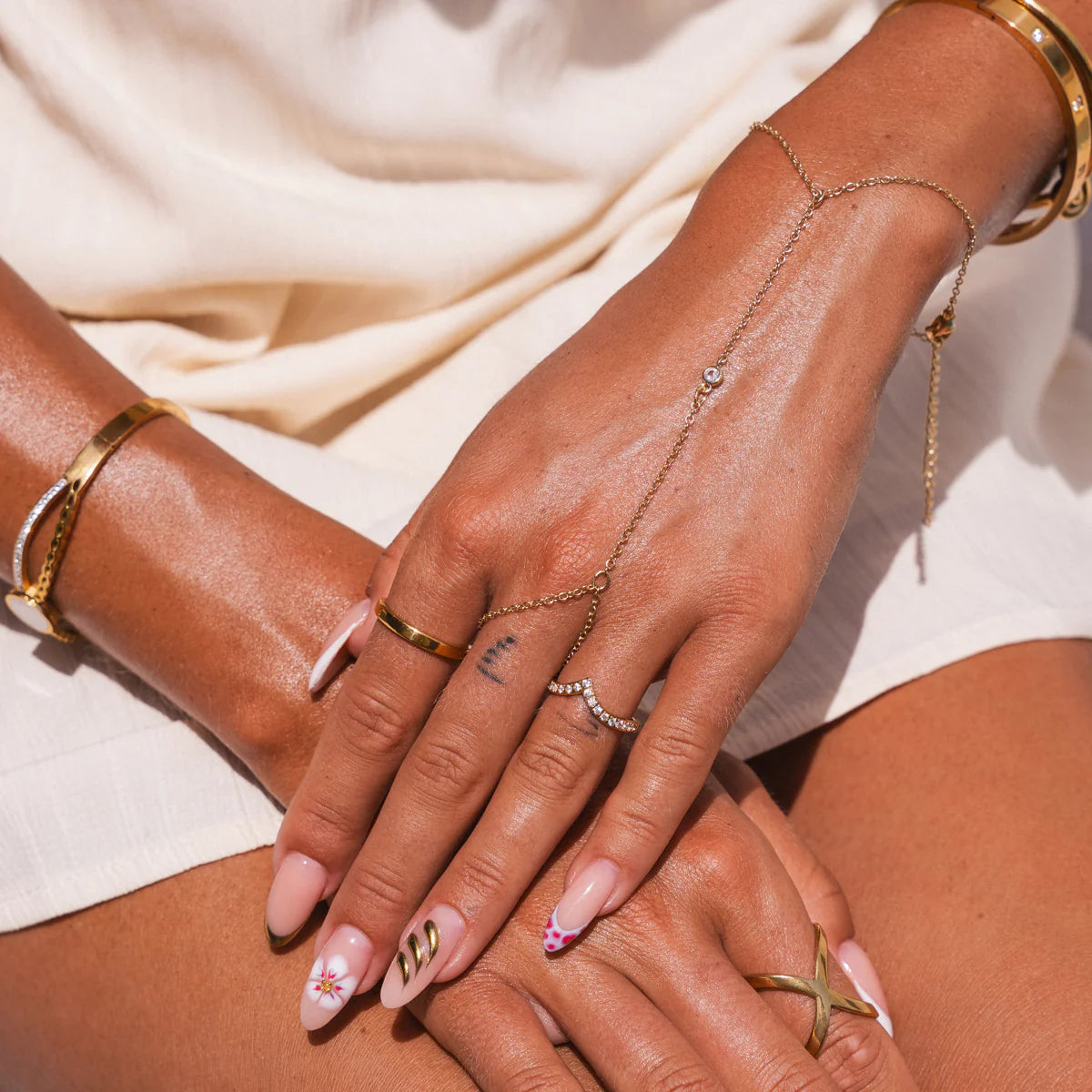 Minimalist hand chain in gold tone with dainty design, worn on hand with layered bracelets and rings. Gold minimalist hand chain for easy styling.