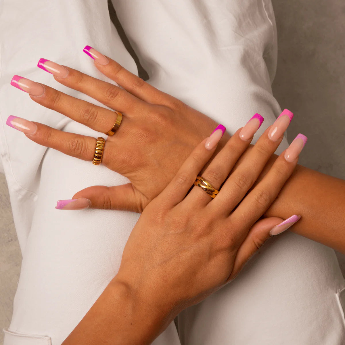Hands wearing gold tone Havana Stack Rings with pink French manicure nails on white pants background