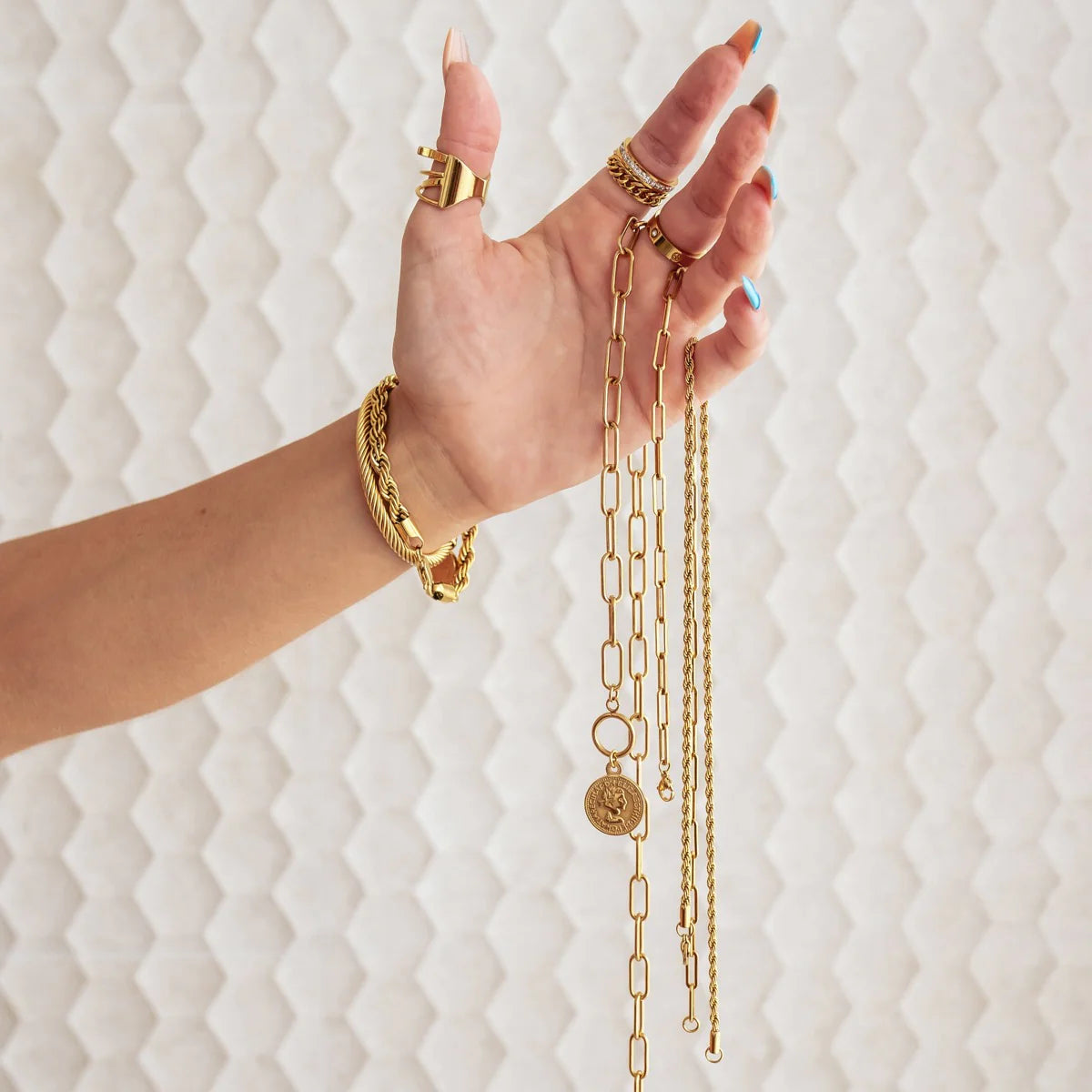 Hand holding gold tone toggle necklace with coin pendant among other gold chains, showcasing its statement appeal and 50cm chain length.