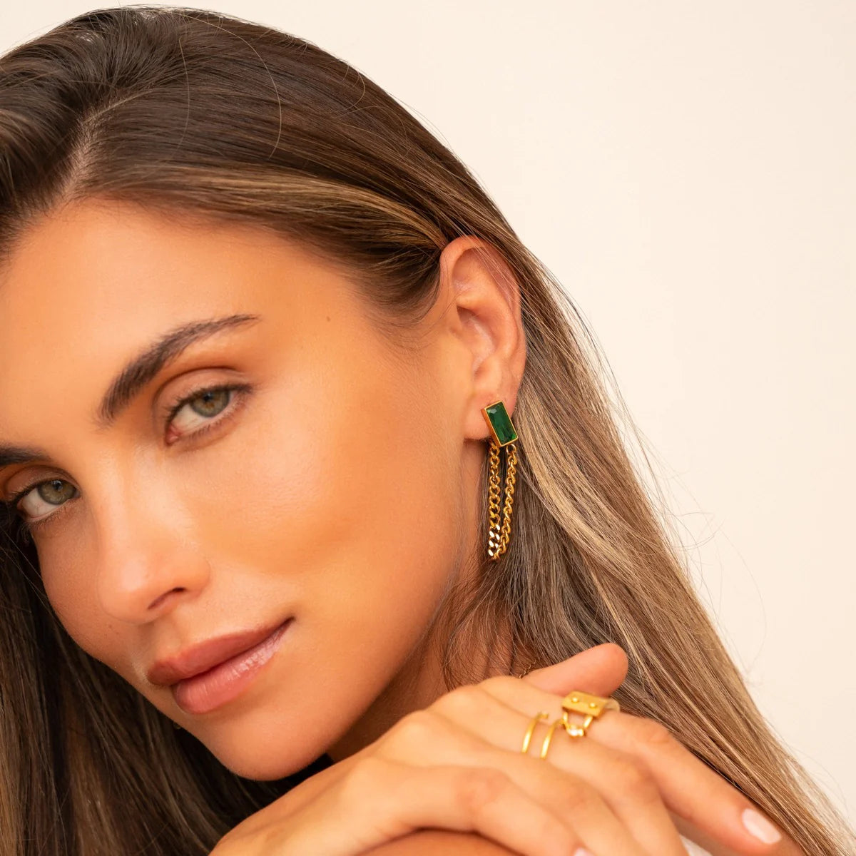 Close-up of Emerald Cuban Earrings on model, featuring green stones and gold-tone chains, ideal for fashion-forward, sensitive-skin wearers.