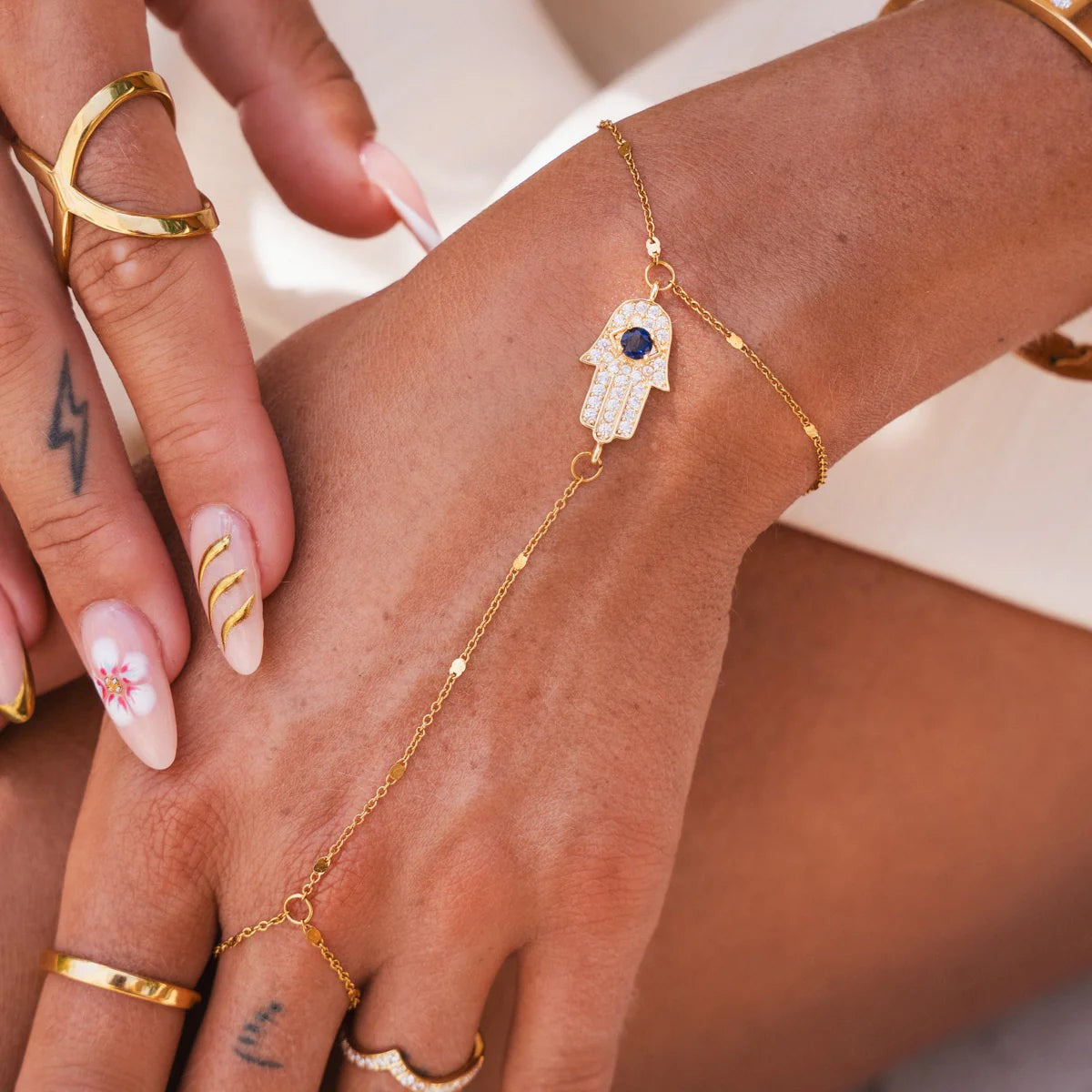 Gold Hamsa hand chain with waterproof design, featuring a blue stone center and delicate link chain, worn on hand for stylish protection.
